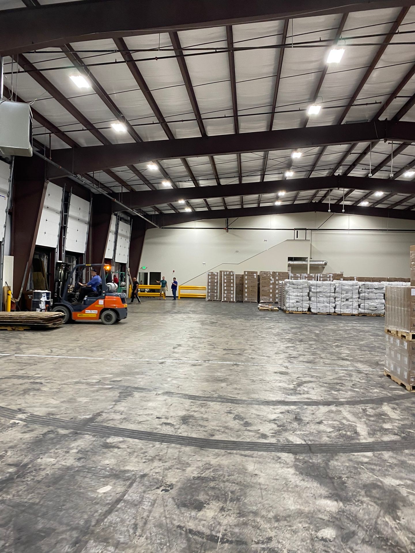 Large warehouse interior with pallets of goods, a forklift in operation, and workers in the background.